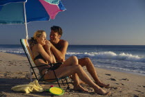 Young couple on sandy beach sitting under a parasol