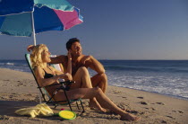 A young couple sitting under a parasol on a sandy beach