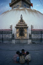 Small group of children with baby crouched together on ground in front of Swayambhu Stupa.