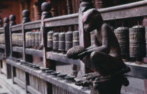 Carving of monkey holding a jack fruit in front of mane or prayer wheels behind.