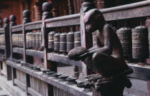 Carving of monkey holding a jack fruit in front of mane or prayer wheels behind.