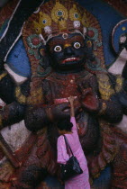 Woman making offerings at the Kala Bhairab or black Shiva in Durbar Square representing the fearsome Tantric form of Shiva in Nepal.