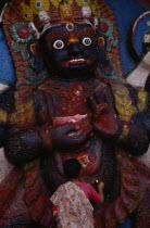 Woman making offerings at the Kala Bhairab or black Shiva in Durbar Square representing the fearsome Tantric form of Shiva in Nepal.