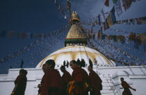 Tibetan families and monks of the Gelug pa sect walking around the Bodhanath stupa during New year festivities.  Lines of prayer flags overhead.