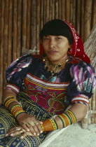 Portrait of a Kuna Indian woman in hammock  with gold jewelry including gold nose ring and rings on fingers  bead design arm bands  wearing brightly coloured layered applique traditional Mola with fin...