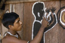 Barasana man  sub group of Tukano  paints front of maloca large communal home. The symbolic shamanic figure is to keep evil spirits and bad weather away.