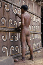 Barasana man  sub group of Tukano  with We body paint  white glass bead necklace  forest seed elbow bands  painting the front of maloca with white and yellow clays and black charcoal for festival