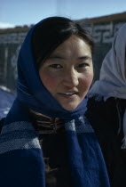 Altai provincial capital in winter. Head and shoulders portrait of young woman wearing fleece lined traditional tunic and modern woollen blue headscarf.East Asia Asian Female Women Girl Lady Mongol U...