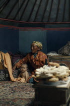 Khalkha winter sheep camp  ger yurt interior with grandmother looking after daughters baby  traditional design wooden boxes for carrying all family posessions when moving from one area of the negdel t...