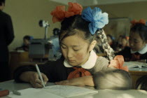 Altai SecondarySchool  11 year old girl writing at desk with her hair plaited and tied with blue and orange bows.East Asia Asian Kids Learning Lessons Mongol Uls Mongolian Teaching