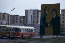 Soviet billboard in central Ulan Bator  depicting Lenin shaking hands with Mongolias first president Sukhebator in urban area with multi-storey apartment blocks behind and buses moving along street.U...