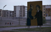 Soviet billboard in central Ulan Bator  depicting Lenin shaking hands with Mongolias first president Sukhebator in urban area with multi-storey apartment blocks behind and people crossing a central sq...