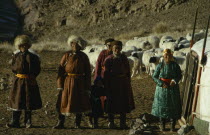 Khalkha winter sheep camp with complete family  father mother daughter grandfather and grandchildren standing outside family ger yurt with sheep in stone walled pen and mountainside in background