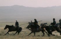 Khalkha horsemen galloping at full stretch to round up wild horses for breaking in  using long lassoe poles.