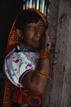 Portrait of older Kuna Indian woman wearing traditional blouse or dulemola with brightly coloured multi-layered mola panel   bead arm and wrist bands  long head scarf against strong sun  and gold nose...