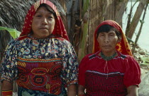 Head and shoulders portrait of Kuna mother and daughter wearing brightly coloured blouses or dulemola with layered applique mola panels and red and yellow head scarves against strong sun.Cuna Caribbe...