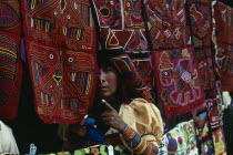 Kuna Indian woman looking out from between brightly coloured applique sewn molas for sale to tourist visitors. Cuna Caribbean American Central America Colored Female Women Girl Lady Hispanic Latin Am...