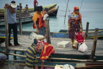 Kuna Indian women wearing brightly coloured traditional mola panel blouses or dulemolas arriving by canoe at island jetty with children.Cuna Caribbean Niadup American Central America Colored Female W...