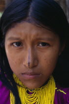 Head and shoulders portrait of Kuna girl from the Arquia community wearing gold nose ring  multi stranded necklace of yellow beads and traditional facial decoration consisting of painted black stripe...