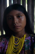 Head and shoulders portrait of Kuna girl from the Arquia community wearing gold nose ring  multi stranded necklace of yellow beads and traditional facial decoration consisiting of black stripe running...