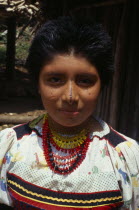Head and shoulders portrait of Kuna girl from the Arquia community wearing small gold nose ring  brightly coloured necklaces and traditional facial decoration including thin painted black line down br...