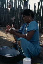 Guajira Indian woman in the process of making "arepas" from kneeded maize flour dough  over a fire in typical open shelter desert home.Wayu Wayuu GuajiroAmerindian Arawakan Colombia-Venezuela border...