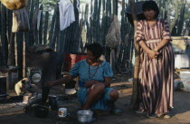 Guajira Indian desert settlement  Two women in familys open shelter-home with small wood fire cooking   possessions hanging on slatted wall and hunting dog in background.Wayu Wayuu GuajroAmerindian...