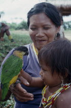 Makuna mother and child with pet parrot.  Both  wearing necklaces of white red and yellow beads.Tukano  Makuna Indian North Western Amazonia family American Children Colombian Columbia Hispanic Indeg...