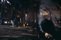 Makuna maloca or communal tribal home interior with smoke rising from open fire toasting coca leaves to be pounded into fine powder  Woman and two standing men in low light.Tukano  Makuna Indian Nort...