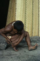 Barasana man removing palm spine from foot outside entrance to maloca/communal home.Tukano sedentary Indian tribe North Western Amazonia American Colombian Columbia Hispanic Indegent Latin America La...