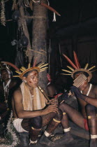 Two Barasana musicians  one with flute the other with panpipes  rest after interminable dancing  both wearing cumare fibre garters and crowns of macaw and toucan feathers. Tukano sedentary Indian tri...