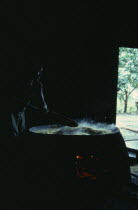 Barasana woman making casabe bread from peeled and grated manioc cooked on large circular shallow clay oven over wood fire enclosed by clay  oven wall. Tukano sedentary Indian tribe North Western Ama...