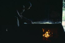 Barasana woman making casabe bread from peeled and grated manioc cooked on large circular shallow clay oven over wood fire enclosed by clay  oven wall.The casabe "bread" must be continually turned and...