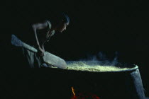 Barasana woman making casabe bread from manioc cooked on large circular shallow clay oven over wood fire enclosed by clay oven wall. Tukano sedentary Indian tribe North Western Amazonia cassava Americ...