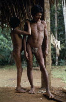 Middle aged Maku nomad standing with his son beside frame of thatched home at base village. indigenous tribe indian nomadic American Colombian Columbia Hispanic Indegent Kids Latin America Latino Mal...