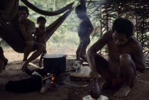 Maku Indian men and children inside palm-thatched shelter/home with hunting dogs lying beside open fire and cooking pot.indigenous tribe indian nomadic American Colombian Columbia Hispanic Indegent K...