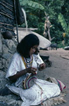 Ika girl outside her home in the Sierra sewing traditional woollen mochila shoulder bag. Wears traditional woven wool&cotton manta cloak and a necklace of many strings of glass beads - a sign of wealt...