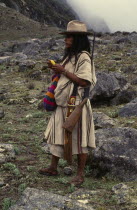 Ika shepherd in the high Sierra carrying rifle on his shoulder  takes lime from his small poporo gourd to place in the wad of coca leaves in his cheek.Lime is the catalyst which releases a very small...