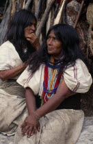 Portrait of Ika mother and daughter in traditional woven wool&cotton mantas cloaks sitting outside their home  daughter de-lousing her mothers hair. Mother wears necklace of red and blue glass beads...