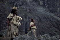 Ika shepherd in traditional wool&cotton manta cloak  carrying newly born lamb walking beside his young sister on mountain pastures high in the Sierra Nevada de Santa Marta.Arhuaco Aruaco indigenous t...