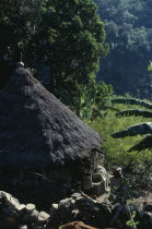 Ika man woman and child outside circular mud-wattle kankurua temple  grass-thatched conical roof with sacred religious pots at apex.In background old stone terraces.Arhuaco Aruaco indigenous tribe Am...