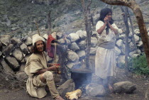 Ika brother and sister in traditional woven wool&cotton mantas cloaks  helmet of woven fique cactus fibre and wool waist belts  cook a potato and mutton sancocho - stew  outside their home using alumi...