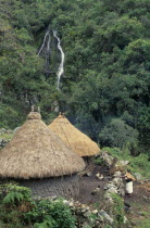 Ika kankurua/ temples in the lower Sierra  circular thatched buildings with sacred potsherds at apices of conical rooves  surrounded by stone wall  Ika man with chickens and pigs outside  small waterf...