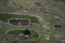 Elevated view over Ika sheep camp with circular thatched huts and stone walled sheep pens high in Sierra Nevada de Santa Marta  N.Colombia.  Flock of sheep graze beside stream  potato crop surrounds h...