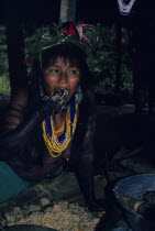 Young Embera daughter painted with black dye extracted from Jagua fruit wearing multiple bead necklaces and head-dress of wild hybiscus and lilies  masticates maize  the saliva sets off fermentation...