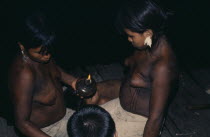 Young Embera daughters of the household painting their bodies with black dye extracted from the indedible Jagua fruit in preparation for curing ceremony - their mother has fever Pacific coastal regio...