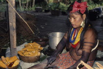 Young Embera woman  body painted with black dye extracted from Jagua fruit wearing multiple bead necklaces  trade-cloth skirt and hair band adorned with hybiscus flowers  prepares corn cobs to make ch...