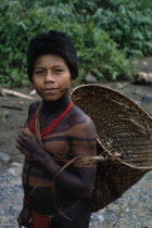 Portrait of young Embera with lower face and body painted with black dye extracted from the Jagua fruit wearing red glass bead necklace  returns from chagra family cultivation patch with manioc roots in woven cane basket .Pacific coastal region tribe body decoration American Colombian Colombia Hispanic Indegent Latin America Latino South America Pacific coastal region tribe body decoration American Colombian Columbia Hispanic Indegent Latin America Latino South America Immature One individual Solo Lone Solitary 1 Single unitary Young Unripe Unripened Green