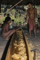 Two Embera men discuss final shaping of wooden dug-out canoe on floor of thatched shelter beside their riverside home.Pacific coastal region boat canoa tribe American Colombian Colombia Hispanic Inde...