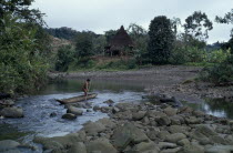 Embera man using pole to steer wooden dug out canoe along river  approaches the port of his stilted and thatched family home set back amongst cleared trees and vegetation.Pacific coastal region boat...